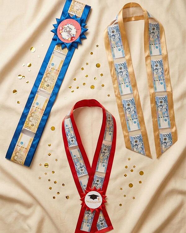 Money lei collection — red money lei, blue money sash, and gold money stole with Philippine peso bills and custom rosette accents